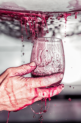 juice splashing from grape press to fall on stemless wine glass held in a man's hand