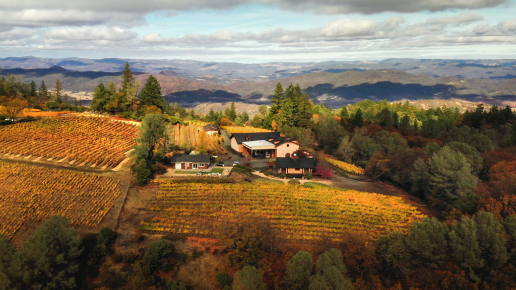panoramic view of Robert Craig winery at the top of Howell mountain, surrounded by fall vineyards with mountains and clouds in the background