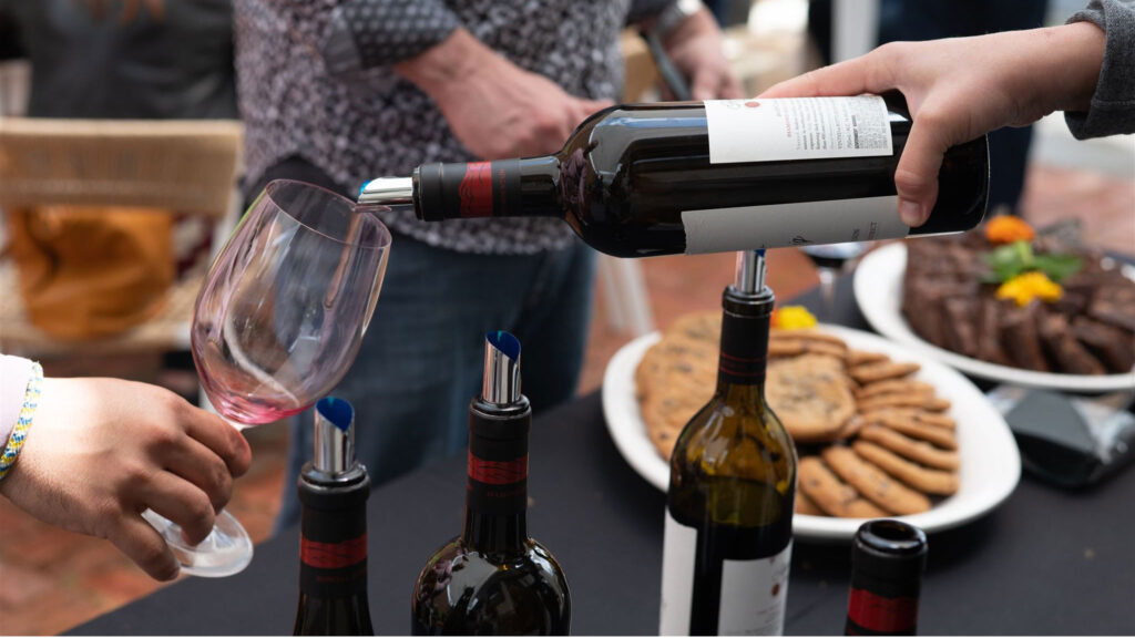 HAND POURING RED WINE OUT OF ROBERT CRAIG WINE BOTTLE WITH COOKIES IN BACKGROUND